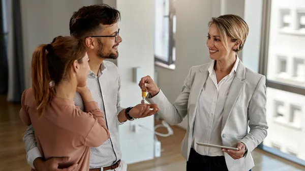 1759474229-happy-real-estate-agent-giving-keys-couple-who-is-buying-their-new-home