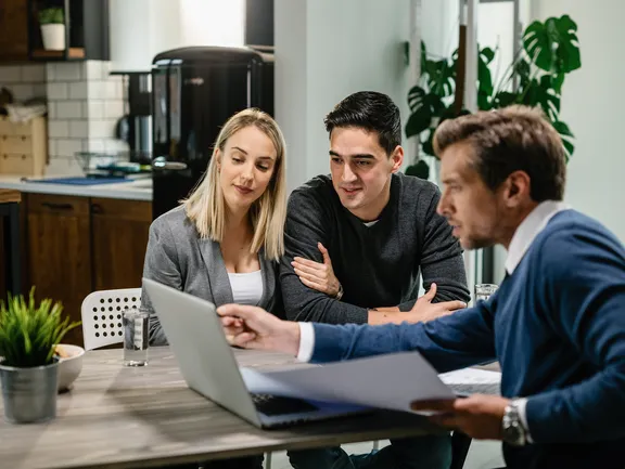 Young couple real estate agent using laptop while going through housing plan meeting